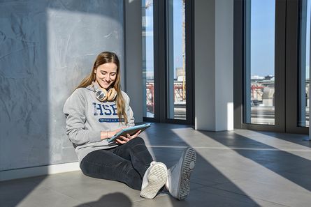 Schülerin sitzt auf Boden im HKIC mit Tablet in der Hand